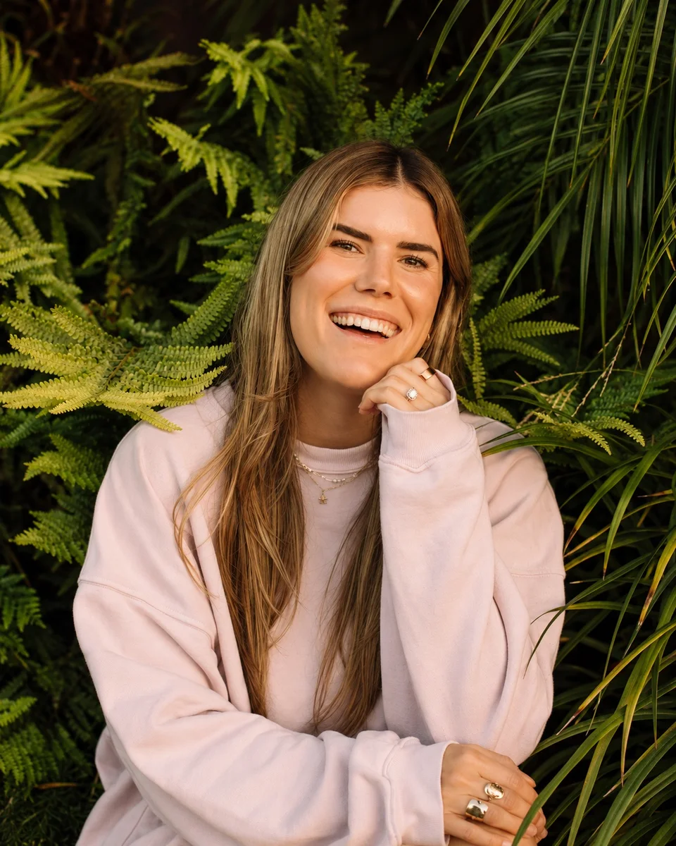 Cambria Joy smiling among palms and ferns.